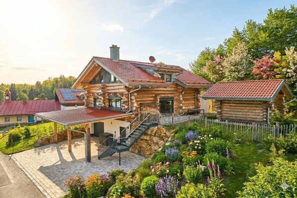 A log cabin with a covered patio, a staircase, and a garden with various plants.