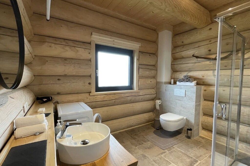 A log cabin bathroom with a window, a sink, a toilet, and a shower.