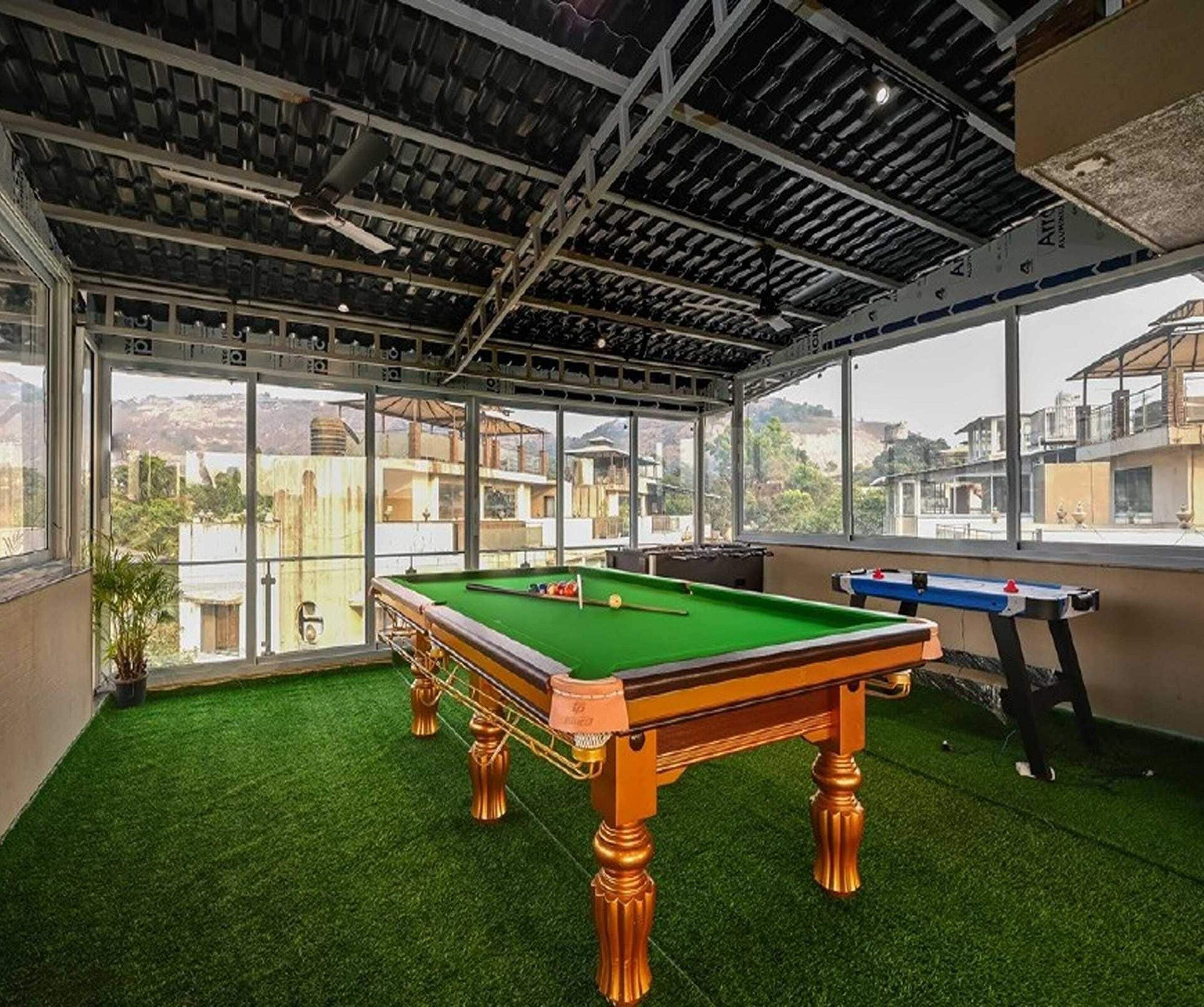 A pool table with a green felt surface, surrounded by a room with a high ceiling and large windows.
