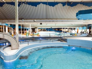 An indoor swimming pool with a slide, seating areas, and a covered roof. - Beach Resort Kamperland - 167 (Kamperland)