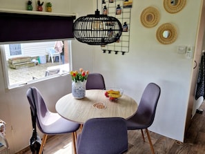 A dining area with a round table, four chairs, a vase with flowers, a bowl of fruit, and a hanging light fixture. - Beach Resort Kamperland - 167 (Kamperland)