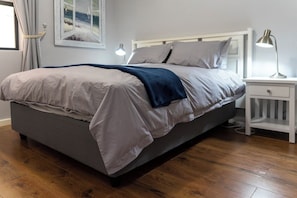 Ein Schlafzimmer mit einem Bett, einem Nachttisch, einer Lampe und einem Fenster mit Vorhängen.