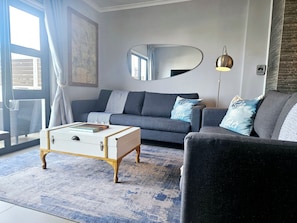 Ein modernes Wohnzimmer mit einem grauen Sofa, einem weißen Couchtisch und einem großen Spiegel an der Wand.