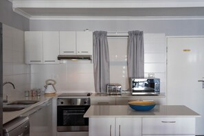 Une cuisine moderne avec des armoires blanches, un four encastré, un four à micro-ondes, un grille-pain et un saladier bleu posé sur le plan de travail.