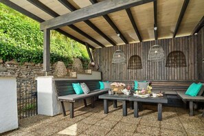 Ein Sitzbereich im Freien mit einer Steinsäule, Holzbänken und einem für eine Mahlzeit gedeckten Tisch.