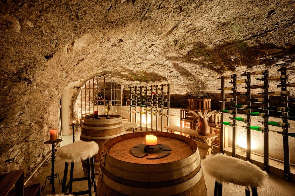 An underground room with stone walls, wooden barrels, and a candle-lit table.