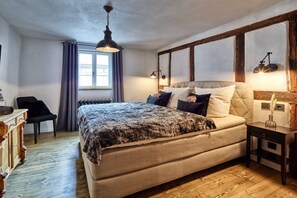 A bedroom with a large bed, a wooden floor, a window with curtains, a nightstand, and a lamp. - Old wine press house (Bernkastel-Kues)