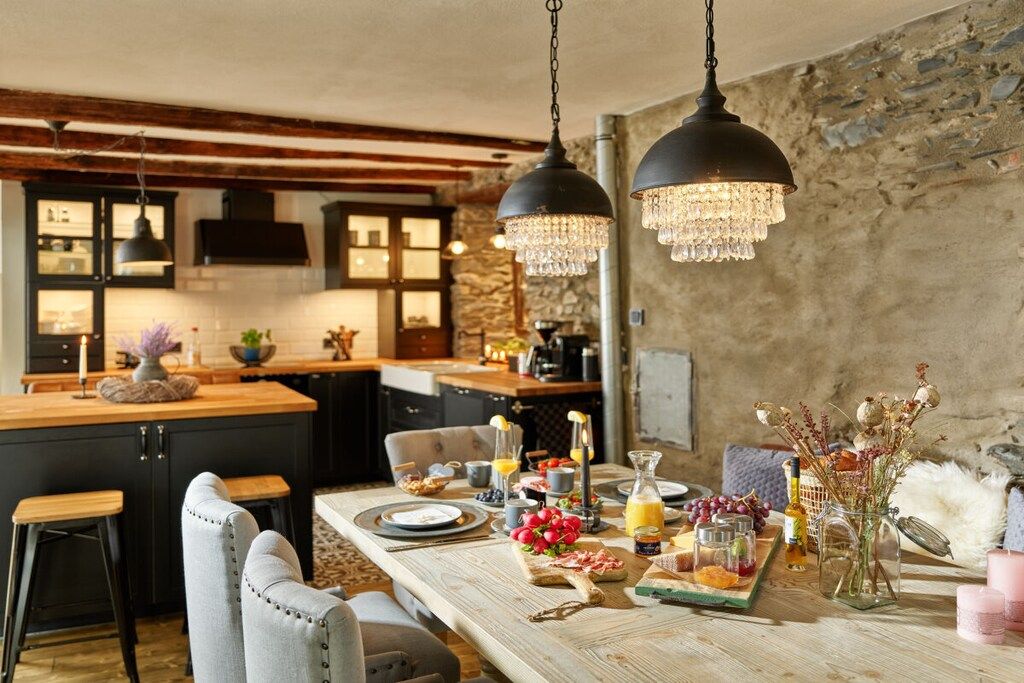 A dining area with a wooden table set for a meal, bar stools, and a kitchen in the background.