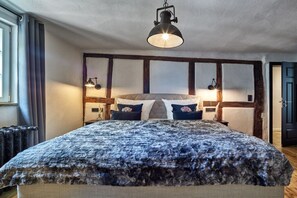 A bedroom with a large bed, a hanging light fixture, and a window with curtains. - Old wine press house (Bernkastel-Kues)