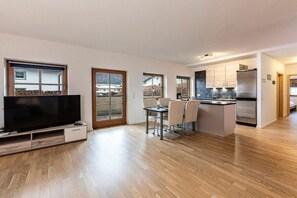 A modern kitchen with a built-in island, a dining area with a table and chairs, and a flat-screen TV on a stand. - Leni holiday apartment (Bischofswiesen)