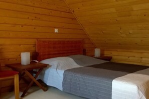 A single-occupancy room with a sloped ceiling, a bed with a gray and white duvet, a wooden nightstand with a white object, and a red chair. - by the sea between Paimpol and Bréhat (ploubazlanec)