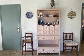 Um quarto com porta fechada, duas cadeiras de madeira, uma estante rosa e duas pratos decorativos na parede.