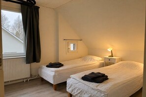 A small, cozy room with two single beds, a nightstand with a lamp, a window with curtains, and a radiator. - Holiday home in Älmhult with swimming pool (Älmhult)