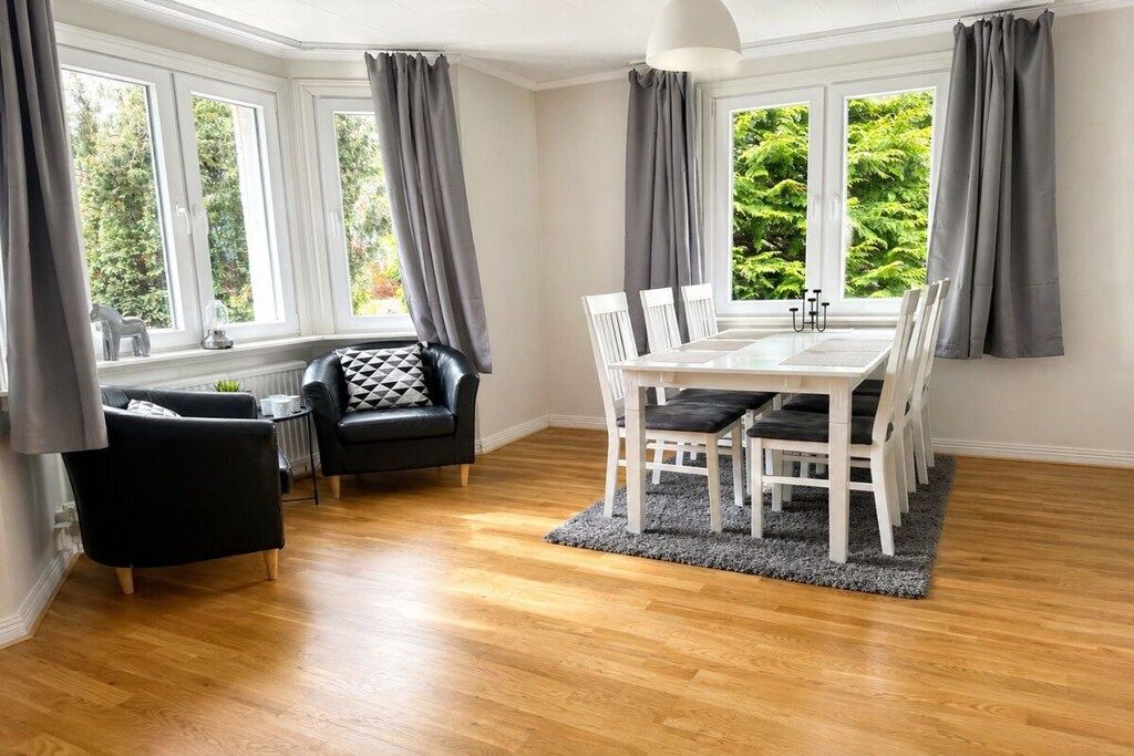 A dining area with a white table and chairs, grey curtains, and a view of greenery outside.