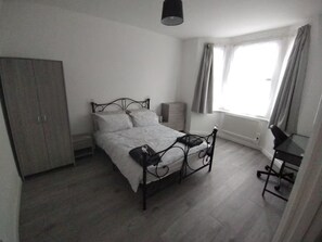 Een slaapkamer met een bed, kast, bureau en raam.