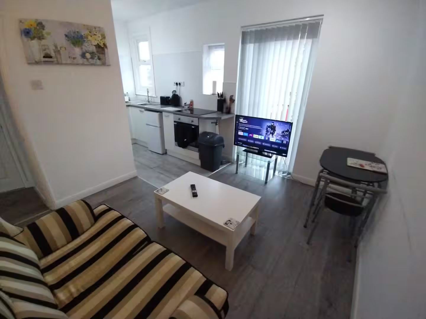 A living room with a striped sofa, a coffee table, a TV, and a small dining area with a table and chairs.