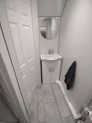 Een kleine badkamer met een witte deur, een ronde spiegel boven een wastafel en een handdoek aan de muur.
