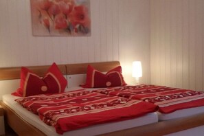 A bed with red bedding and pillows, a wooden headboard, and a wall painting. - Holiday apartment with 2 bedrooms (Saarburg)