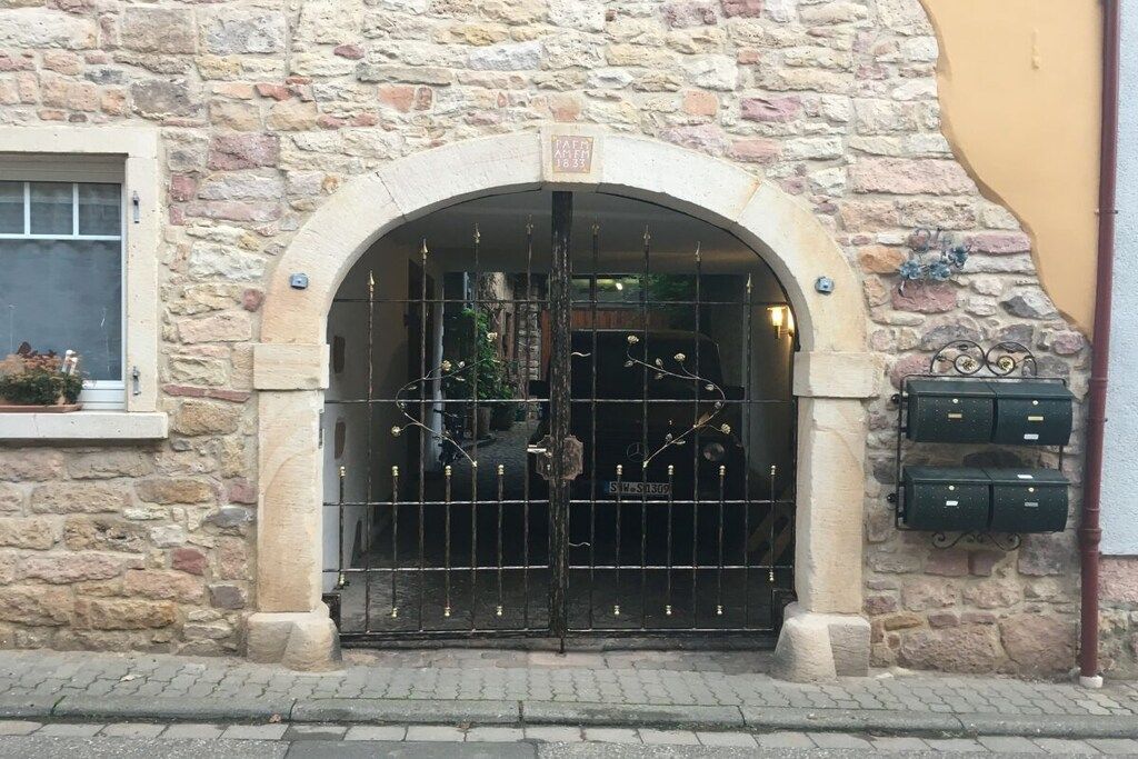 Ein Steinhaus mit großem Bogenportal, einem Metallgitter und einem kleinen Fenster mit einer Pflanze.