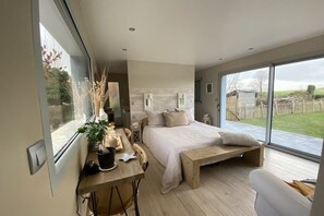 Ein modernes Schlafzimmer mit einem großen Bett, einem Holztisch und Blick ins Freie.