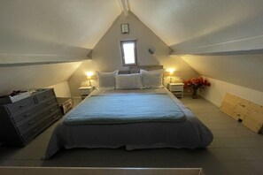 Een slaapkamer met een bed, nachtkastjes, een dressoir, een raam en een vaas met bloemen.