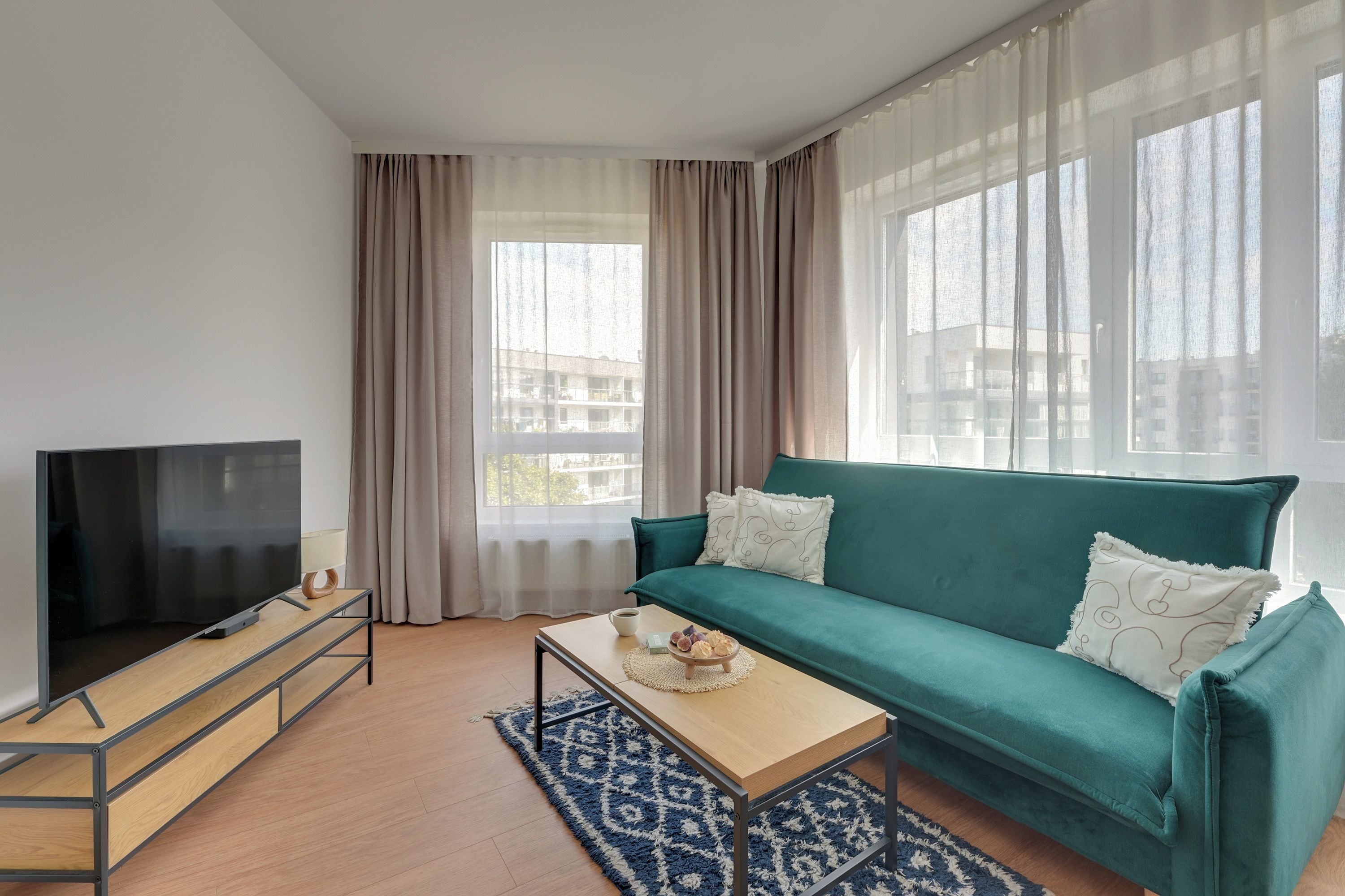 Ein modernes Wohnzimmer mit Fernseher, einem blaugrünen Sofa und einem Couchtisch.