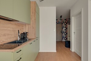 A modern kitchen with a wooden countertop, a coffee machine, and a patterned wall in the background. - Przymorze Śląska Business & Gym with Free Parking by Downtown Apartments (Gdańsk)