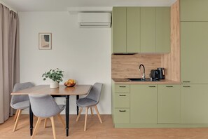 A compact kitchen with a dining area, featuring a table with chairs, a small plant, and a fruit bowl. - Przymorze Śląska Business & Gym with Free Parking by Downtown Apartments (Gdańsk)