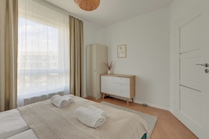 A bedroom with a bed, a wardrobe, a bedside table with a vase, and a framed picture on the wall. - Przymorze Śląska Business & Gym with Free Parking by Downtown Apartments (Gdańsk)
