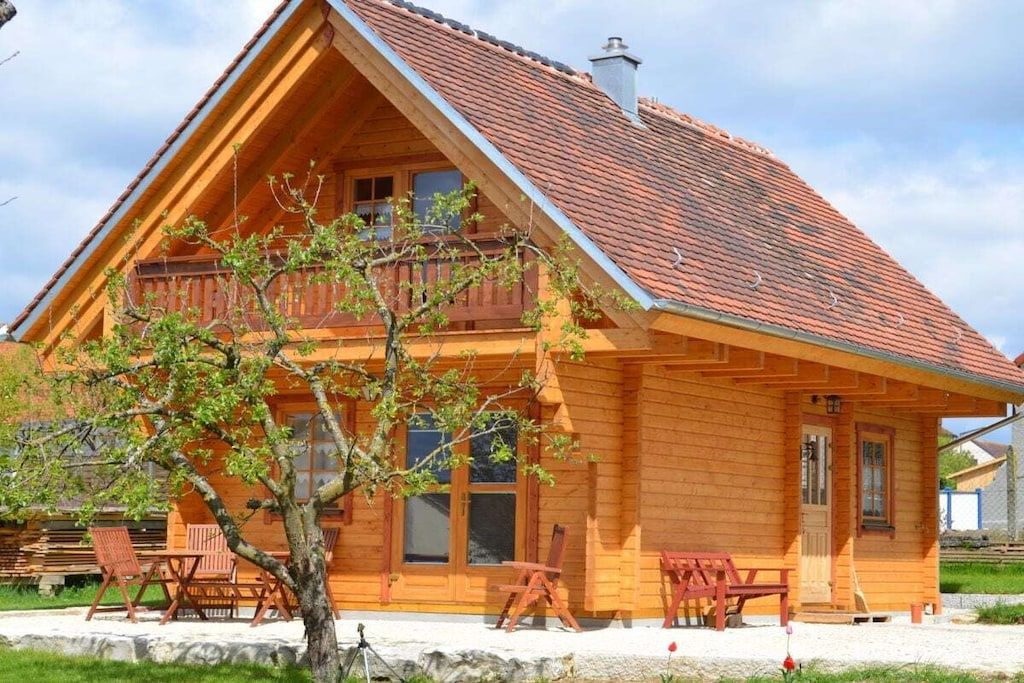 A wooden cabin with a sloped roof, a balcony, and outdoor seating.
