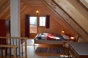A cozy attic bedroom with a wooden sloped ceiling, a bed with a striped rug, two bedside lamps, and a view through a window with curtains. - Holiday home with 1 bedroom (Adelschlag Ortsteil  Möckenlohe)