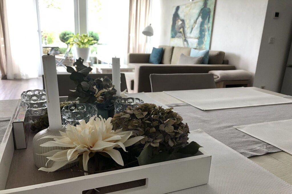 A dining area with a white table set for two, featuring a vase with flowers and a candle.