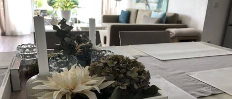 A dining area with a white table set for two, featuring a vase with flowers and a candle.