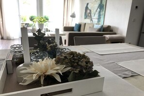 Ein Essbereich mit einem weißen Tisch, gedeckt für zwei Personen, mit einer Blumenvase und einer Kerze.