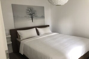 Ein ordentlich bezogenes Bett mit weißen Leinen, einem Kopfteil und einem an der Wand hängenden Baum-Kunstwerk.