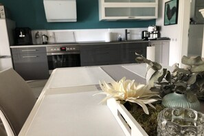 Une cuisine moderne avec des meubles blancs, une machine à café et un coin repas comprenant une table et des chaises blanches.