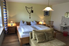 A hotel room with a bed, two bedside tables with lamps, a wooden chair, a sofa, a wall-mounted mirror, and a bathroom with a sink and shower. - 1 - Gertraud Weiderer (Lindberg)