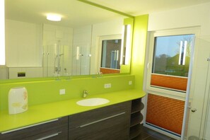 A modern bathroom with a large mirror, a white sink, and a shower area. - 9 in the Villa Meeresblau (Cuxhaven)