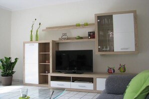 A modern living room with a flat-screen TV, wooden shelving, and a cabinet. - Holiday apartment with 2 bedrooms (Ostbevern)