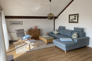 Een moderne woonkamer met een blauwe bank, een houten stoel, een kleine tafel en een hanglamp.
