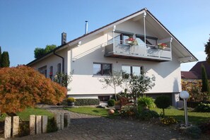 A two-story house with a balcony, a chimney, and a garden with various plants and a pathway. - Herold holiday apartment (Friedrichshafen)