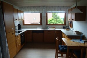 A compact kitchen with wooden cabinets, a built-in dishwasher, and a window providing natural light. - Herold holiday apartment (Friedrichshafen)