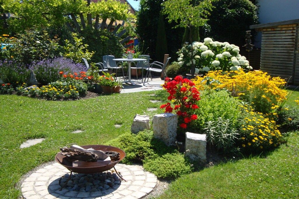 Un jardin agrémenté d’un foyer extérieur, de coins salon et de diverses plantes à fleurs.