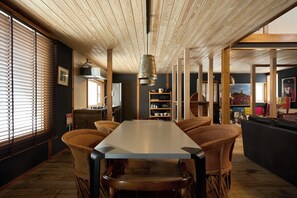 A dining area with a long table, wooden chairs, and a hanging light fixture.