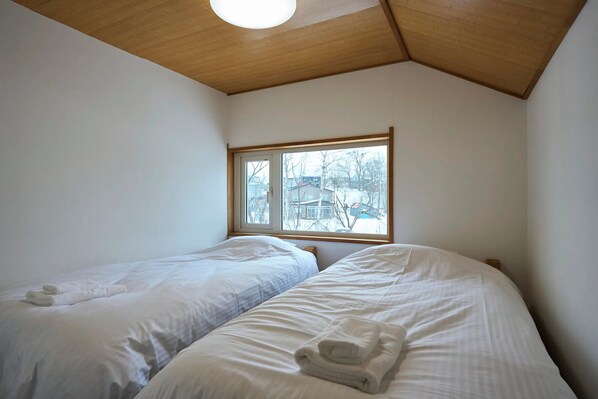 Une chambre avec deux lits, une fenêtre donnant sur des immeubles et un plafond en bois.