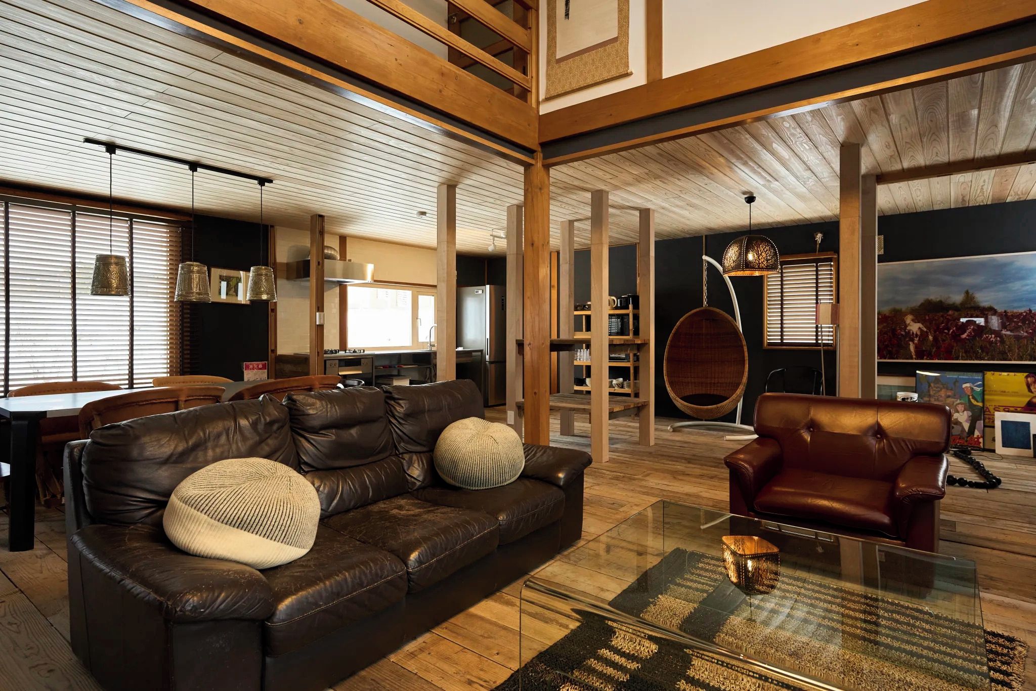 A modern living room with a leather sofa, a glass coffee table, and a hanging chair.