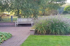 A paved walkway leading to a bench, surrounded by greenery and a fence. - Seedorf Hörster Heide (Warendorf)