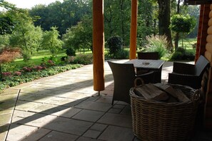 A covered patio with a table and chairs, surrounded by a garden with various plants and trees. - Holiday home in Neuenkirchen with barbecue (Neuenkirchen)