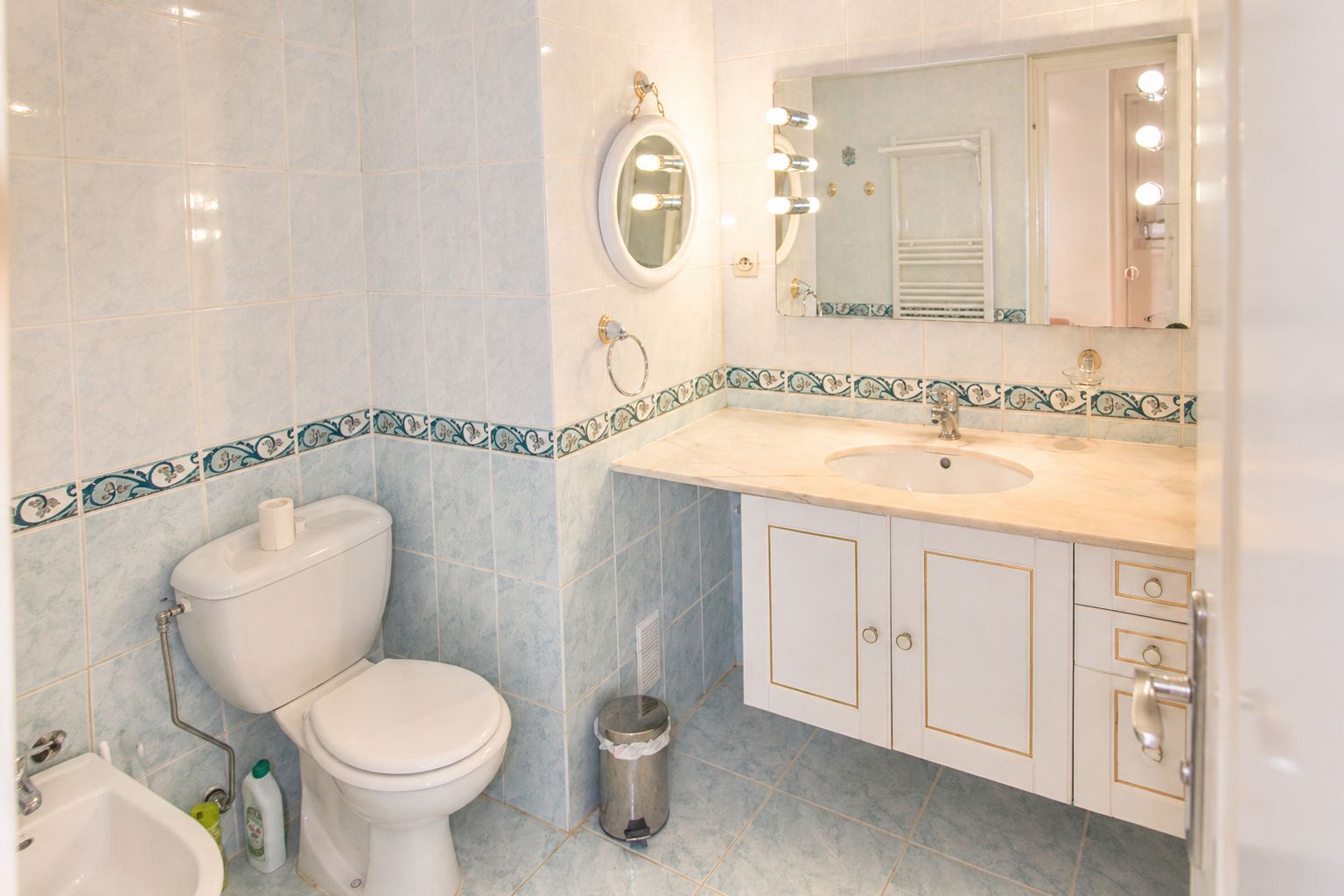 Baño con inodoro, lavamanos, espejo y tocador con armarios.