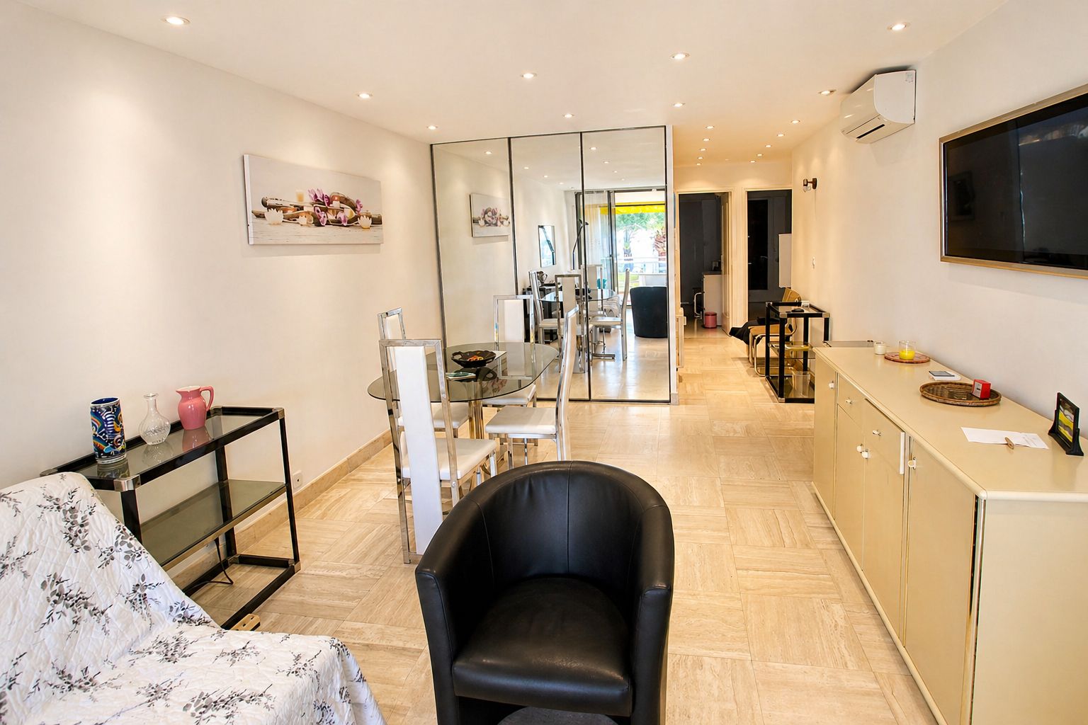 A modern living room with a sofa, a glass dining table, and a kitchen area in the background.